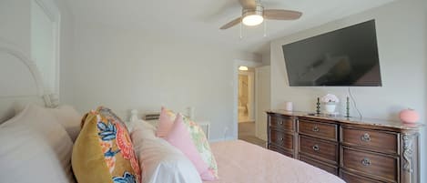 A bedroom with a bed, dresser, ceiling fan, and a TV on the wall.