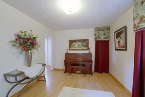 Una habitació amb un piano, un quadre, un ram de flors i una cortina vermella.
