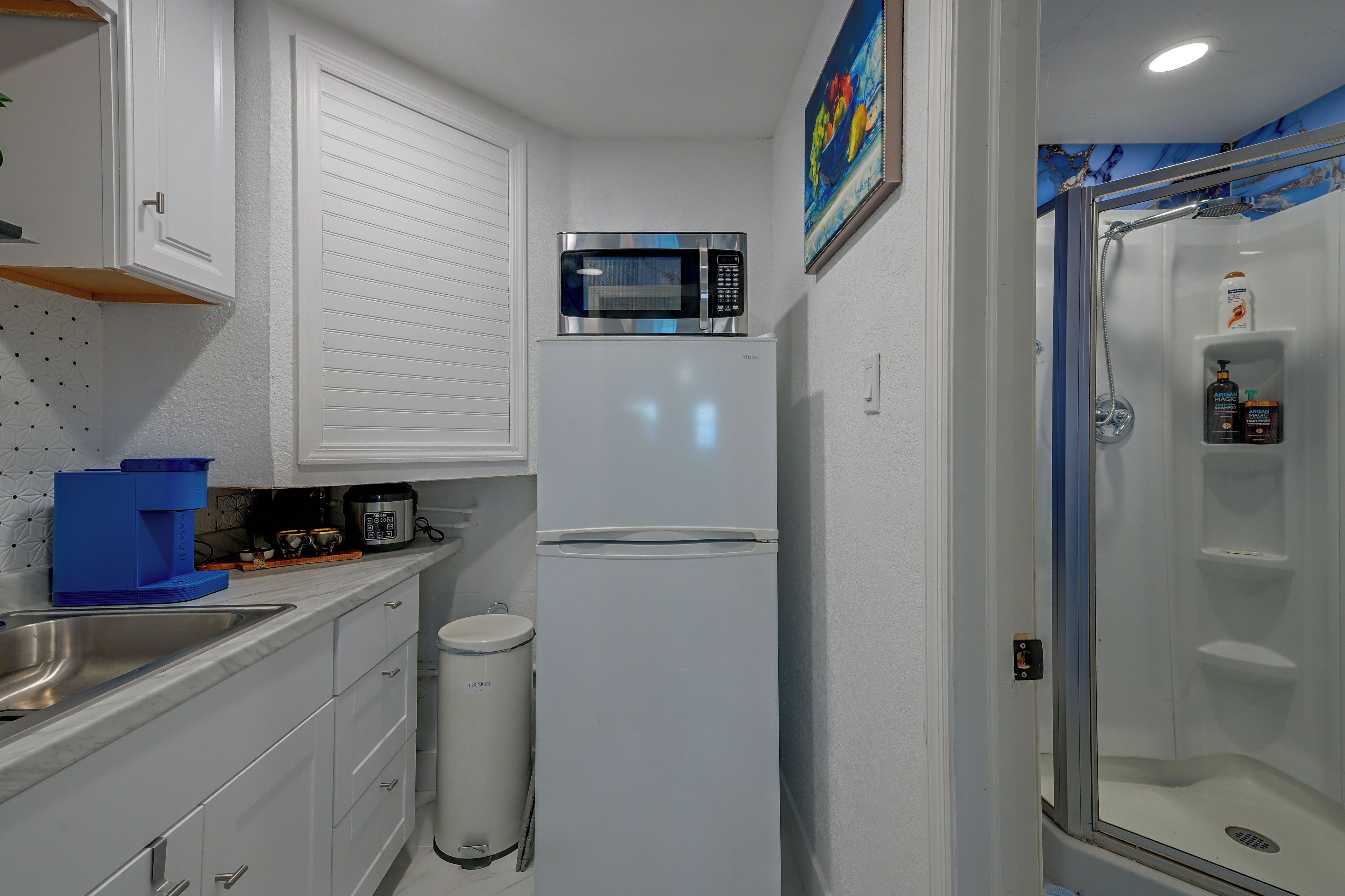 A compact kitchen with a microwave, a sink, and a trash bin.
