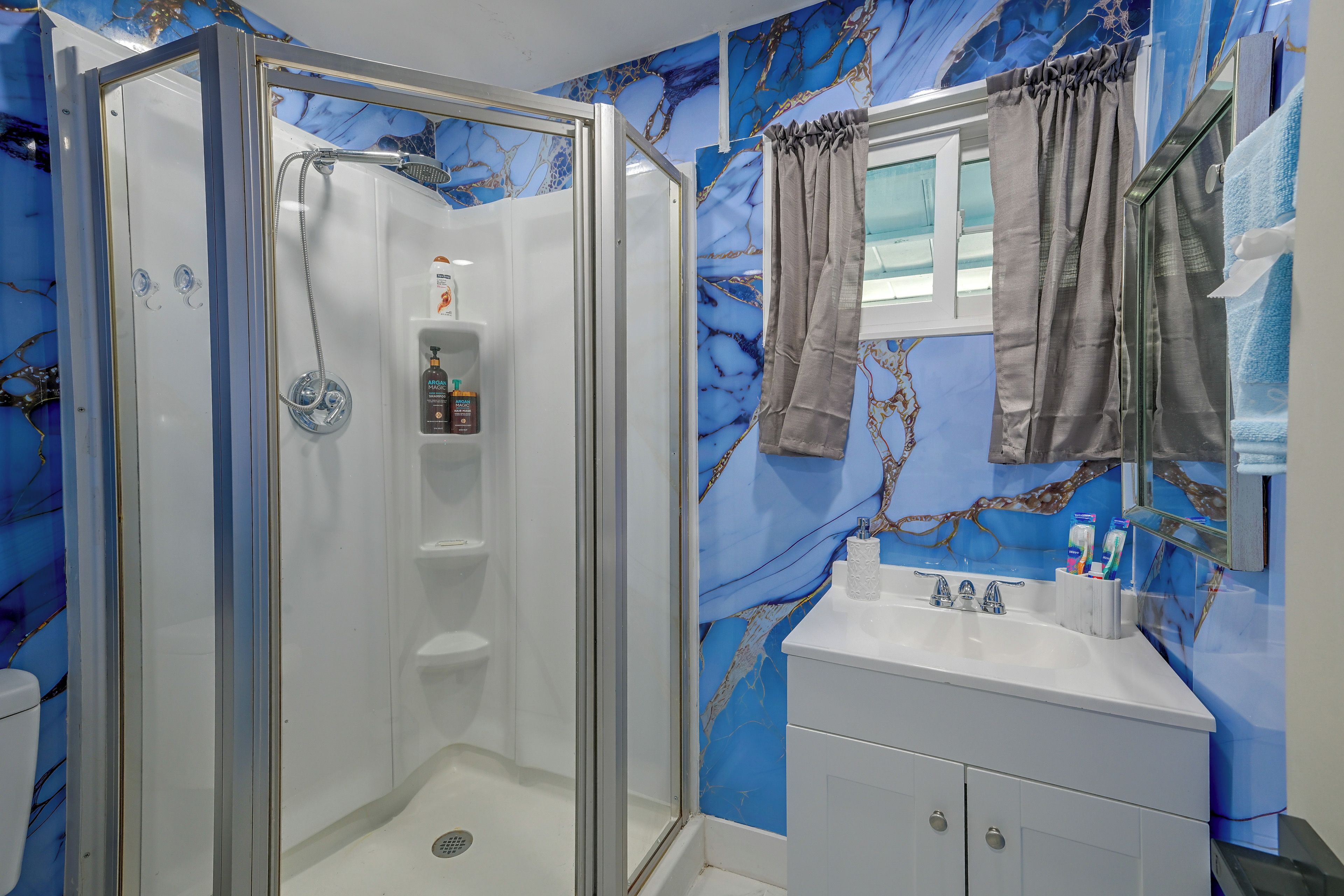 A bathroom with a glass-enclosed shower, a vanity with a mirror, and a marble-patterned wall.