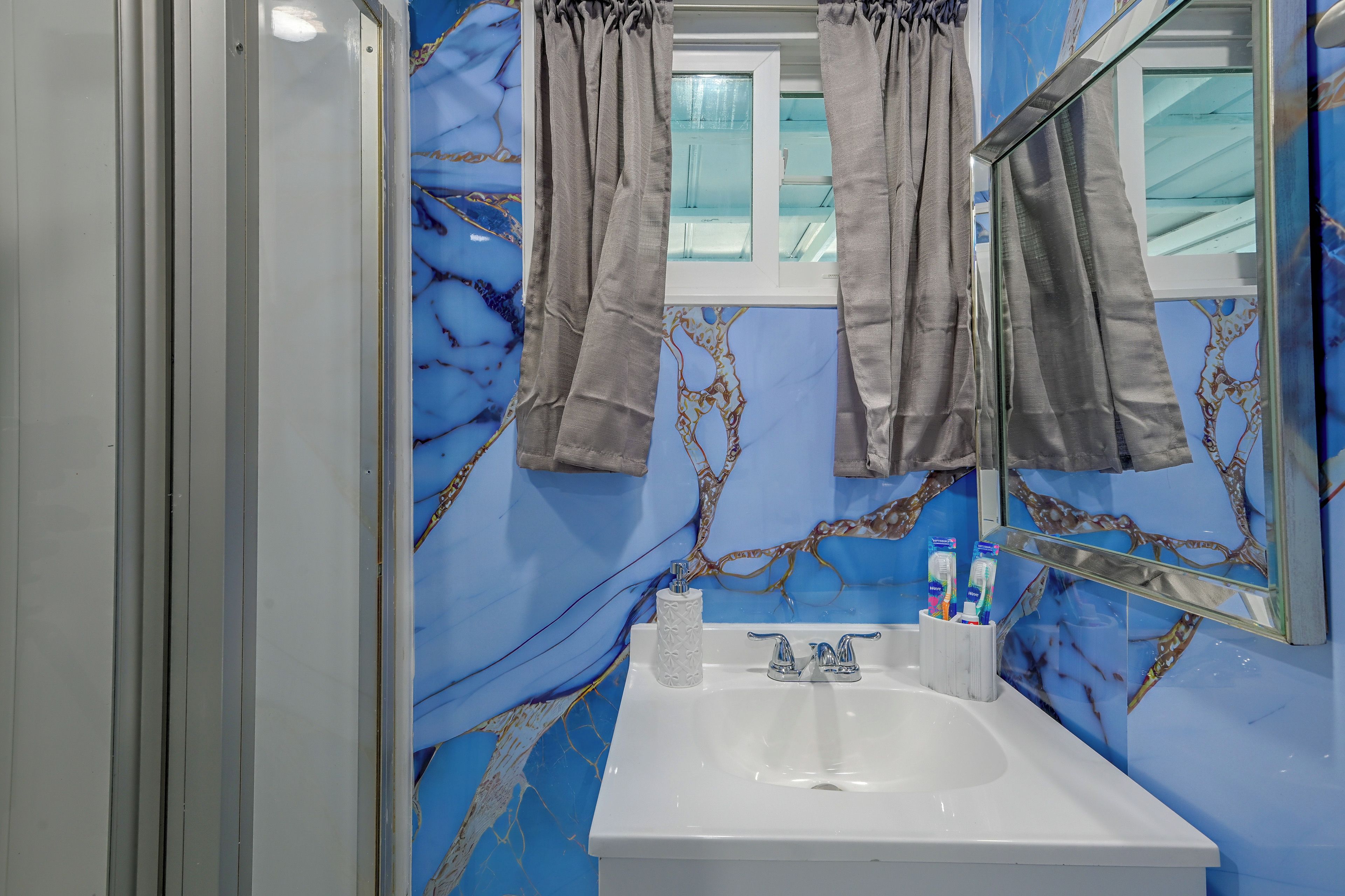 A bathroom with a white sink, a mirror, and a window with curtains.