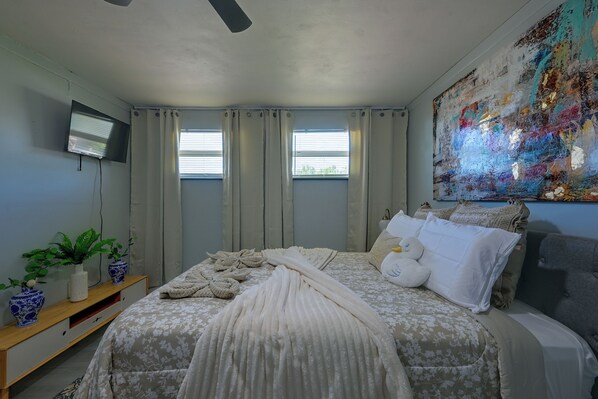 A bedroom with a bed, a TV, a painting, and a window with curtains. - Briza Azul Studio Apartment 3 Mi to Weeki Wache (Spring Hill)