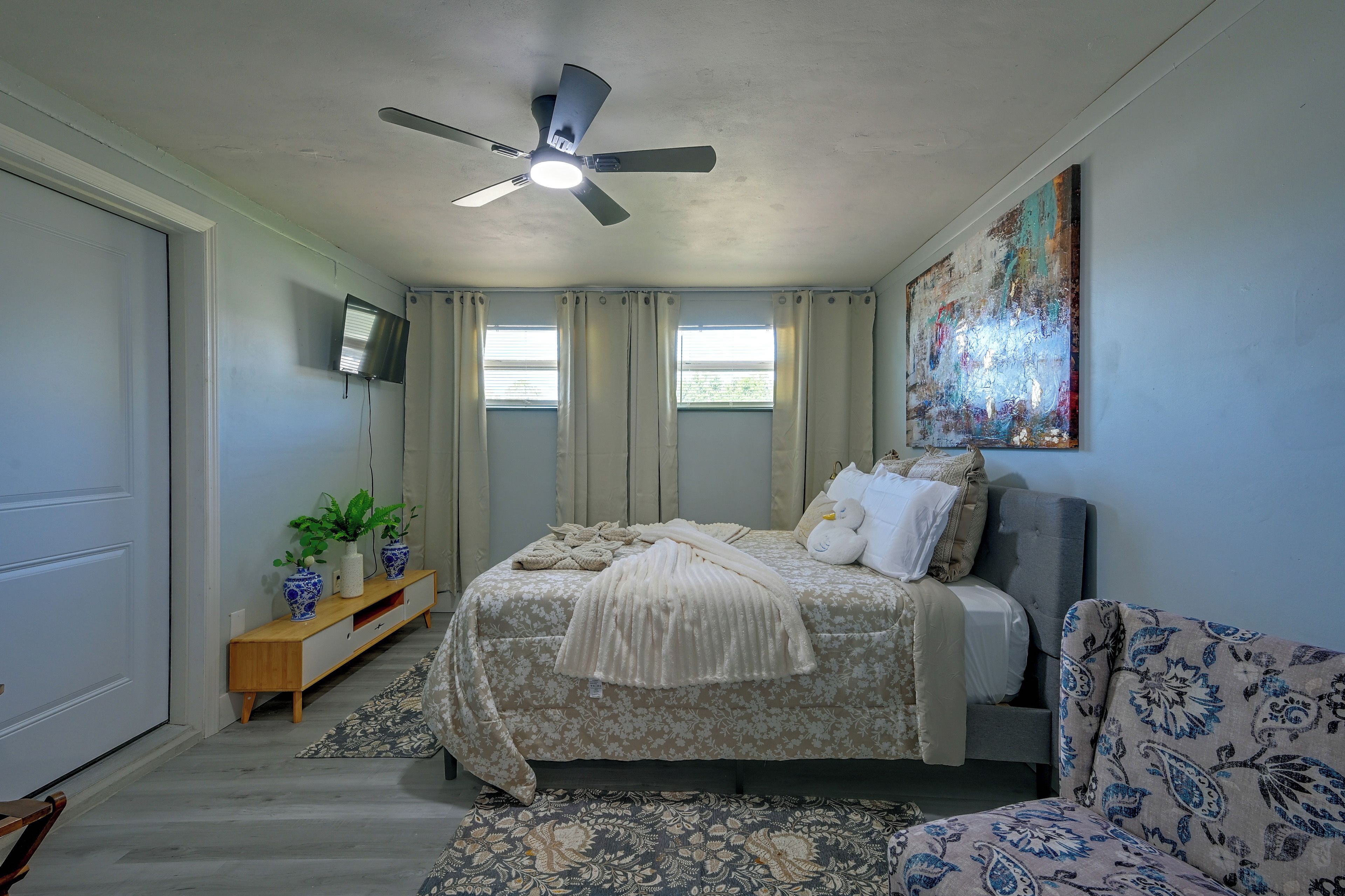 A bedroom with a bed, a sofa, a ceiling fan, a TV, and a painting on the wall.