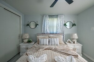 Quarto com uma cama, duas mesas de cabeceira, uma janela com cortinas e dois espelhos fixados na parede.