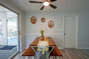 Uma área de refeições com mesa de madeira, bancos e um ventilador de teto. Há relógios fixados na parede e quadros acima da mesa.