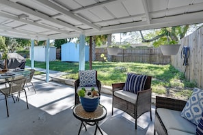 A covered patio area with outdoor furniture, including a table and two chairs, and a hanging plant basket. - Yaya Weeki Wache Gateway 2BR Home w/ Backyard (Spring Hill)