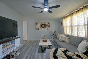 Sala de estar com televisão de tela plana, ventilador de teto, sofá, mesa de centro e um objeto decorativo na parede.