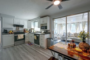 Una cocina moderna con armarios blancos, una estufa negra y un comedor con mesa de madera.