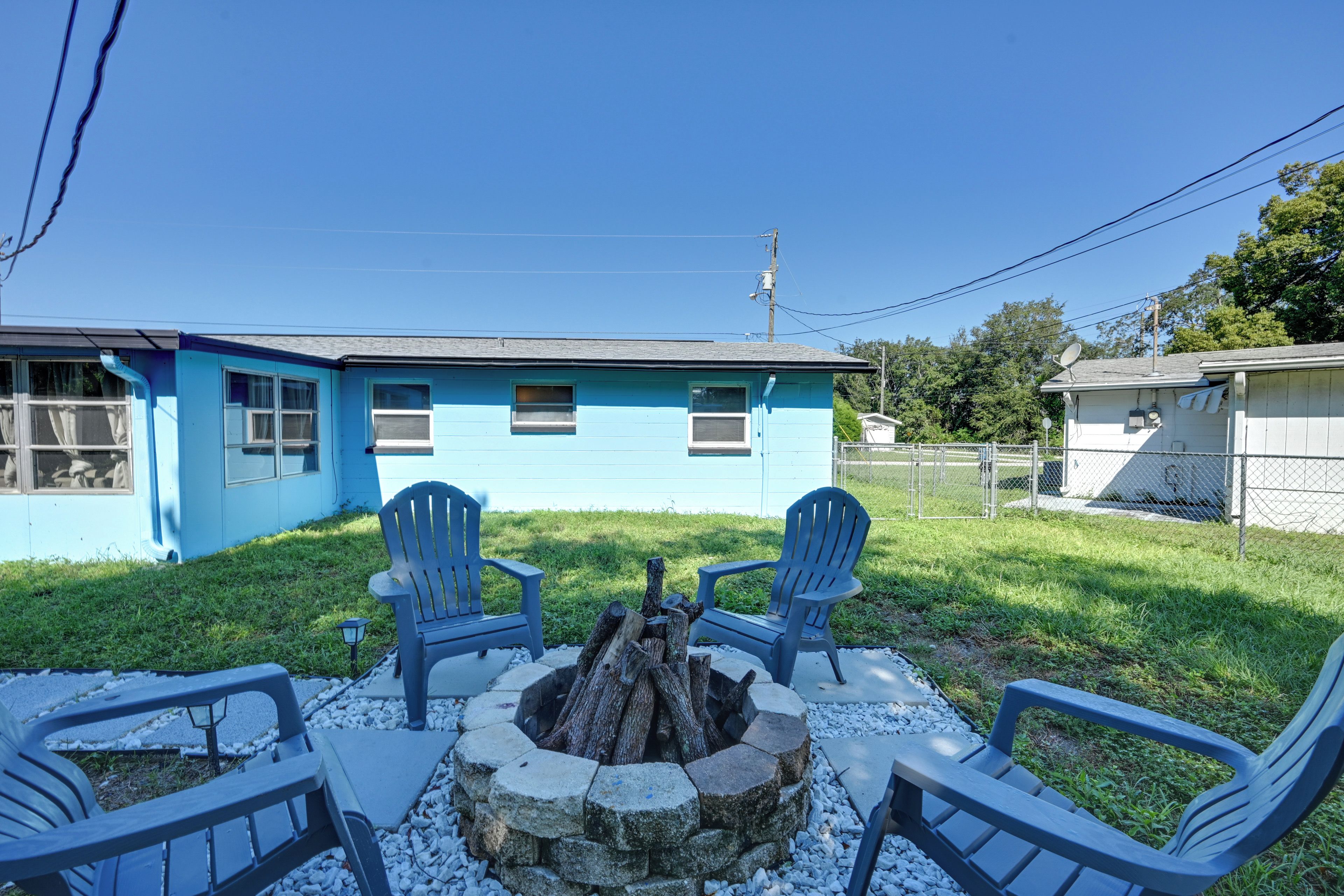 A blue house with a fire pit and two Adirondack chairs in the yard.
