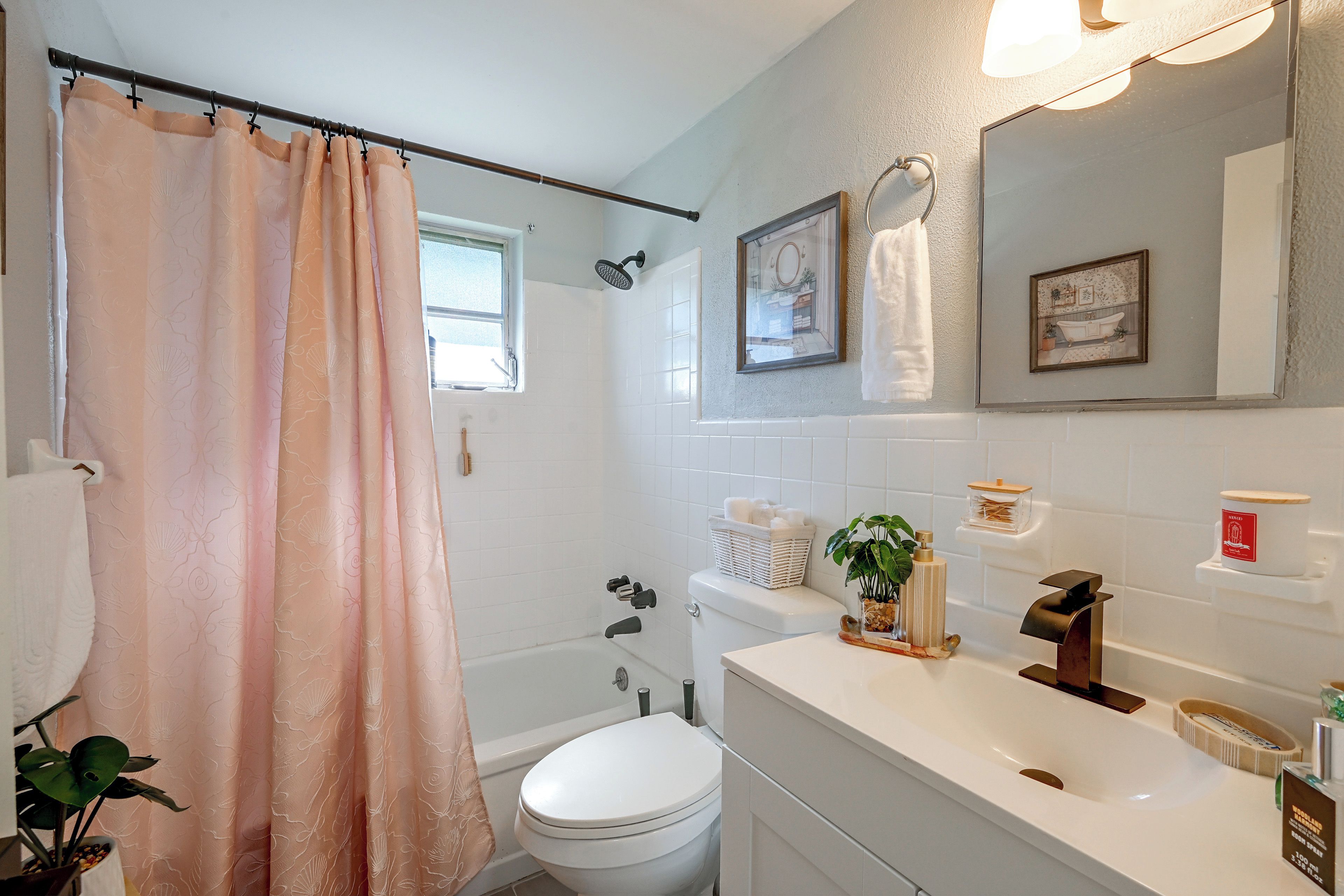 A bathroom with a shower curtain, a toilet, a sink with a soap dispenser, and a mirror.
