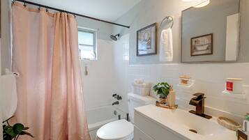 A bathroom with a shower curtain, a toilet, a sink with a soap dispenser, and a mirror.