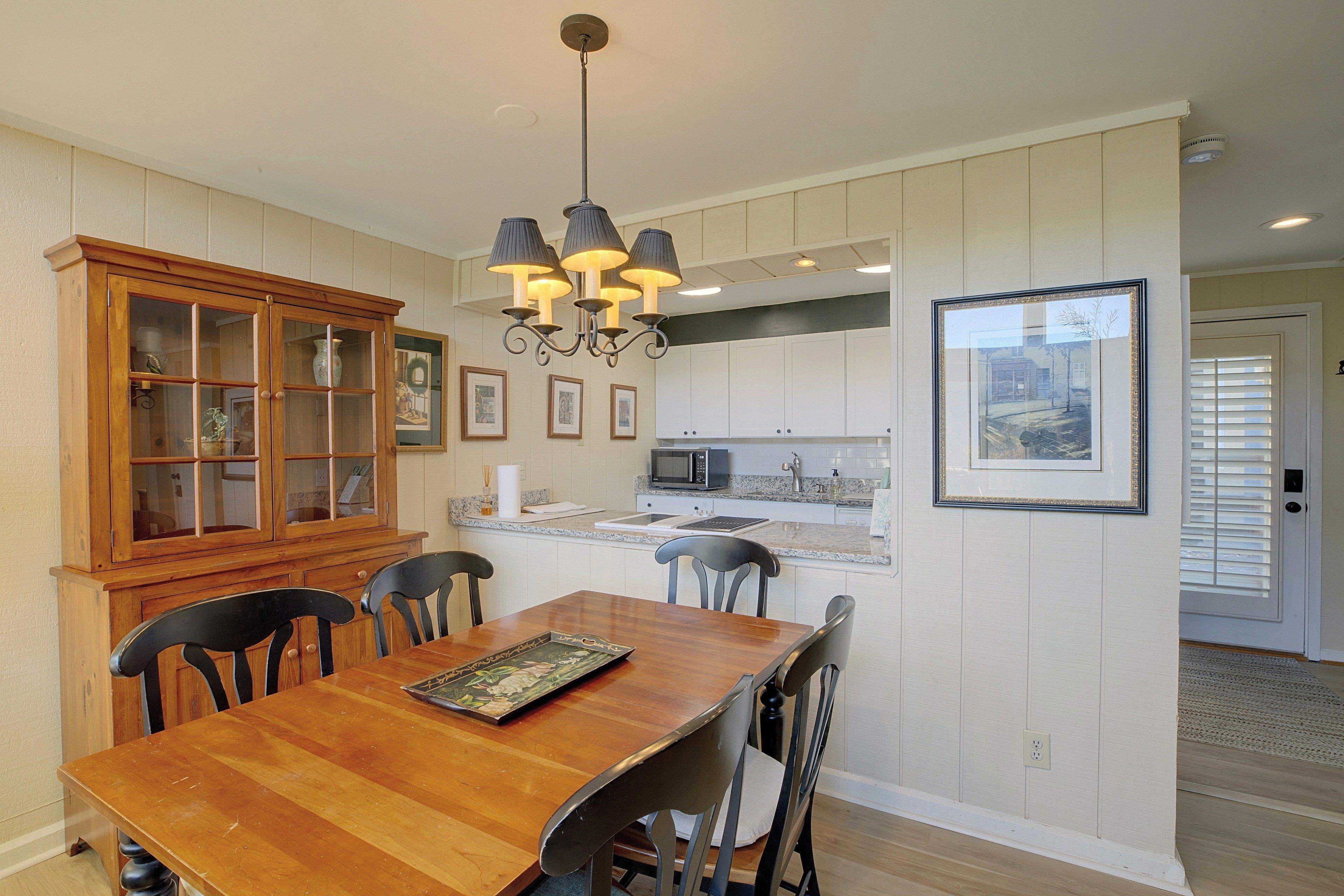 A dining area with a wooden table and chairs, a cabinet with glass doors, and a kitchen in the background.