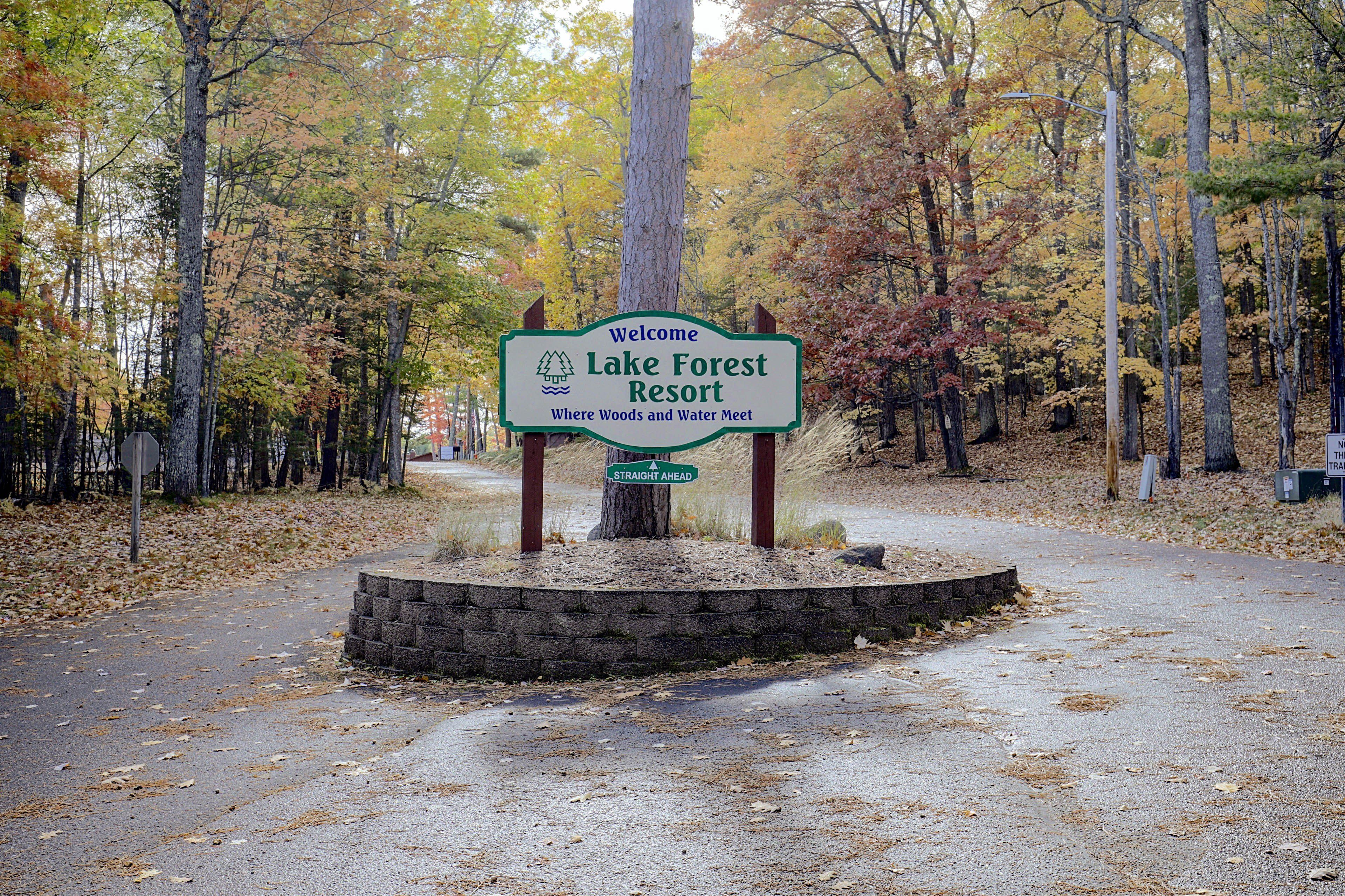 A welcome sign for Lake Forest Resort with a view of a forested area.