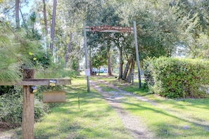 A wooden signpost with a welcome message, a path leading through a wooded area, and a notice sign on the ground.