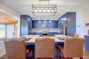 A modern kitchen with blue cabinets, a central island, and a dining area with brown chairs.