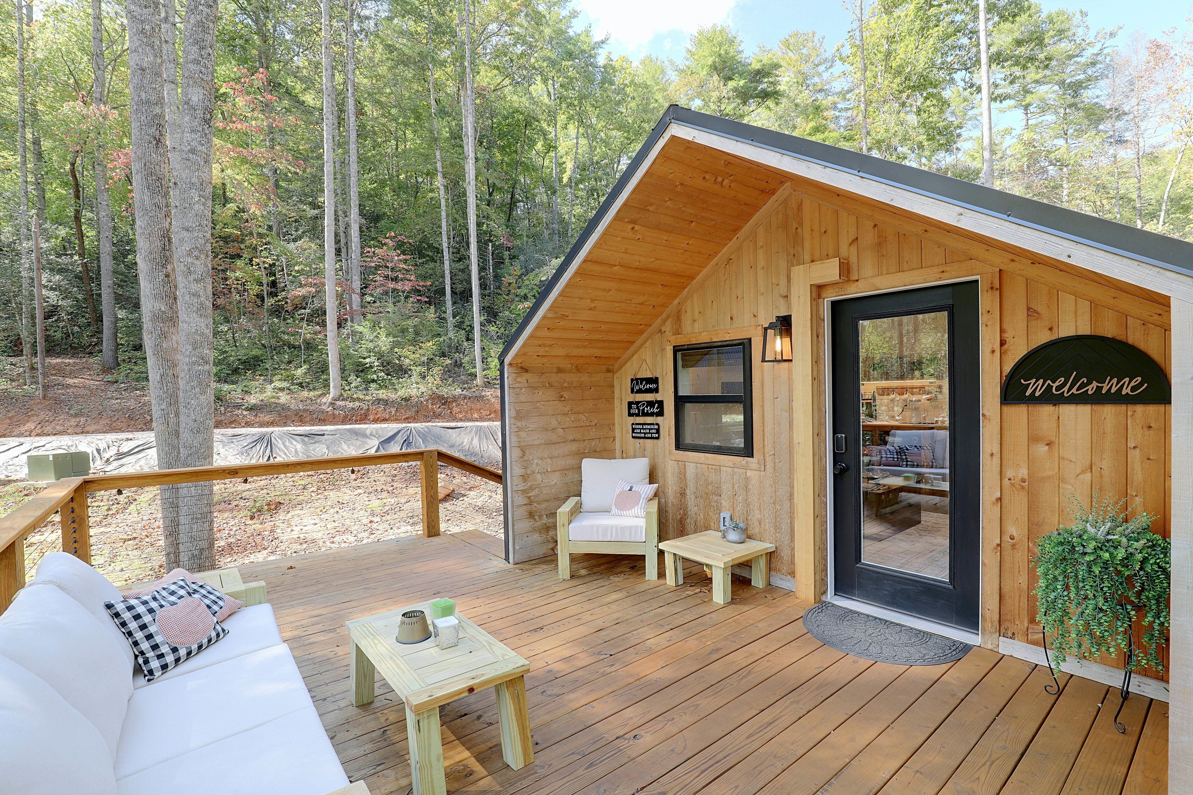 Una cabaña de madera con terraza, un sofá, una mesa y un cartel de bienvenida.