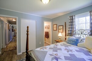 A bedroom with a bed, a nightstand, a lamp, a window with curtains, and a door leading to another room.
