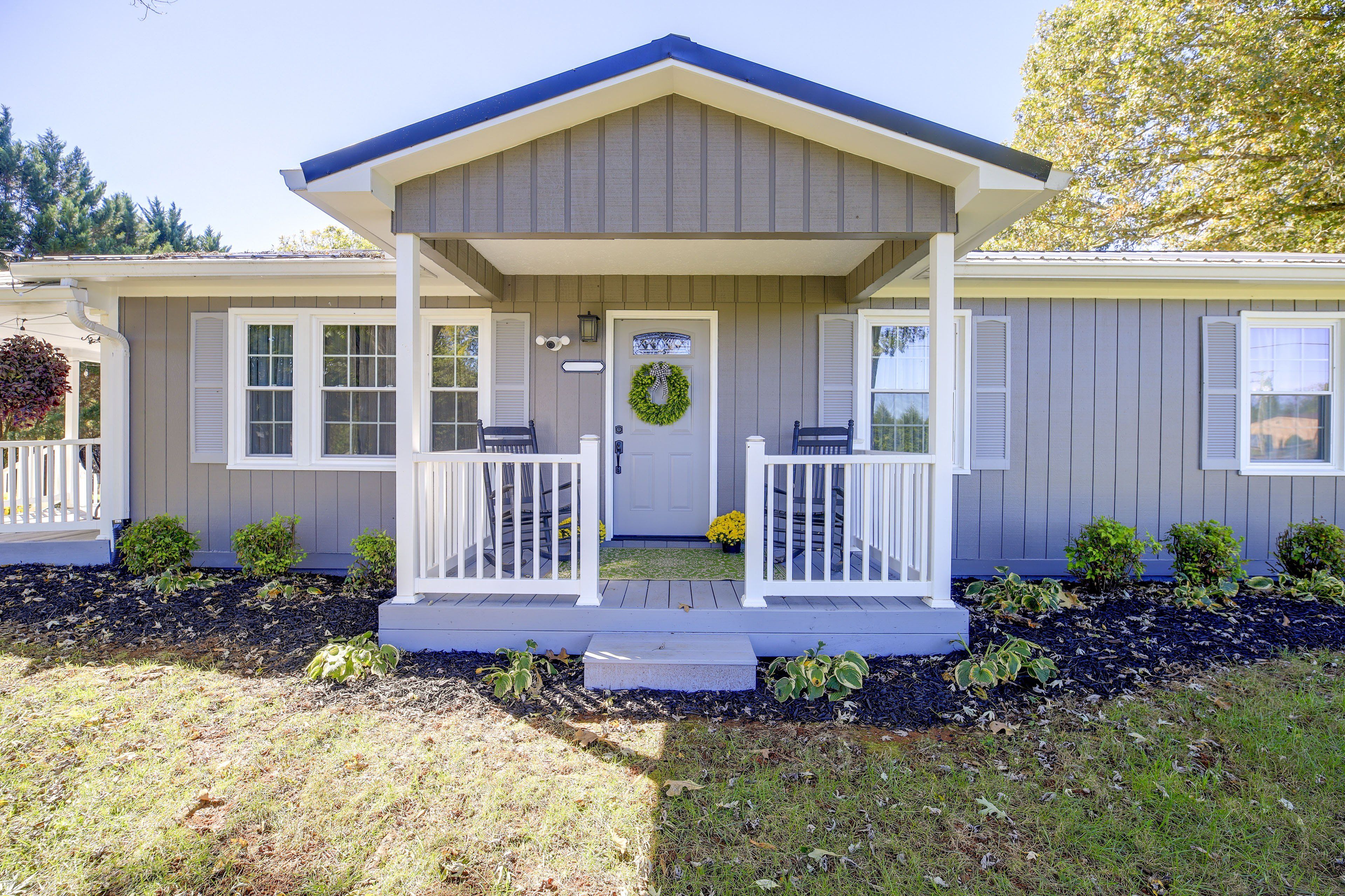 A single-story house with a front porch, a door with a wreath, and a small garden area with mulch and plants.