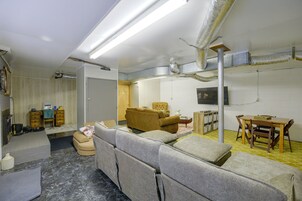 A furnished living room with a sofa set, a dining table with chairs, a television mounted on the wall, and a fireplace with a mantel.