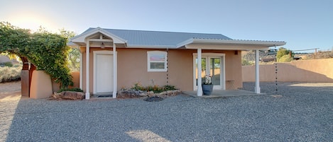 A single-story house with a covered porch, a front door, and a small garden area with a potted plant.