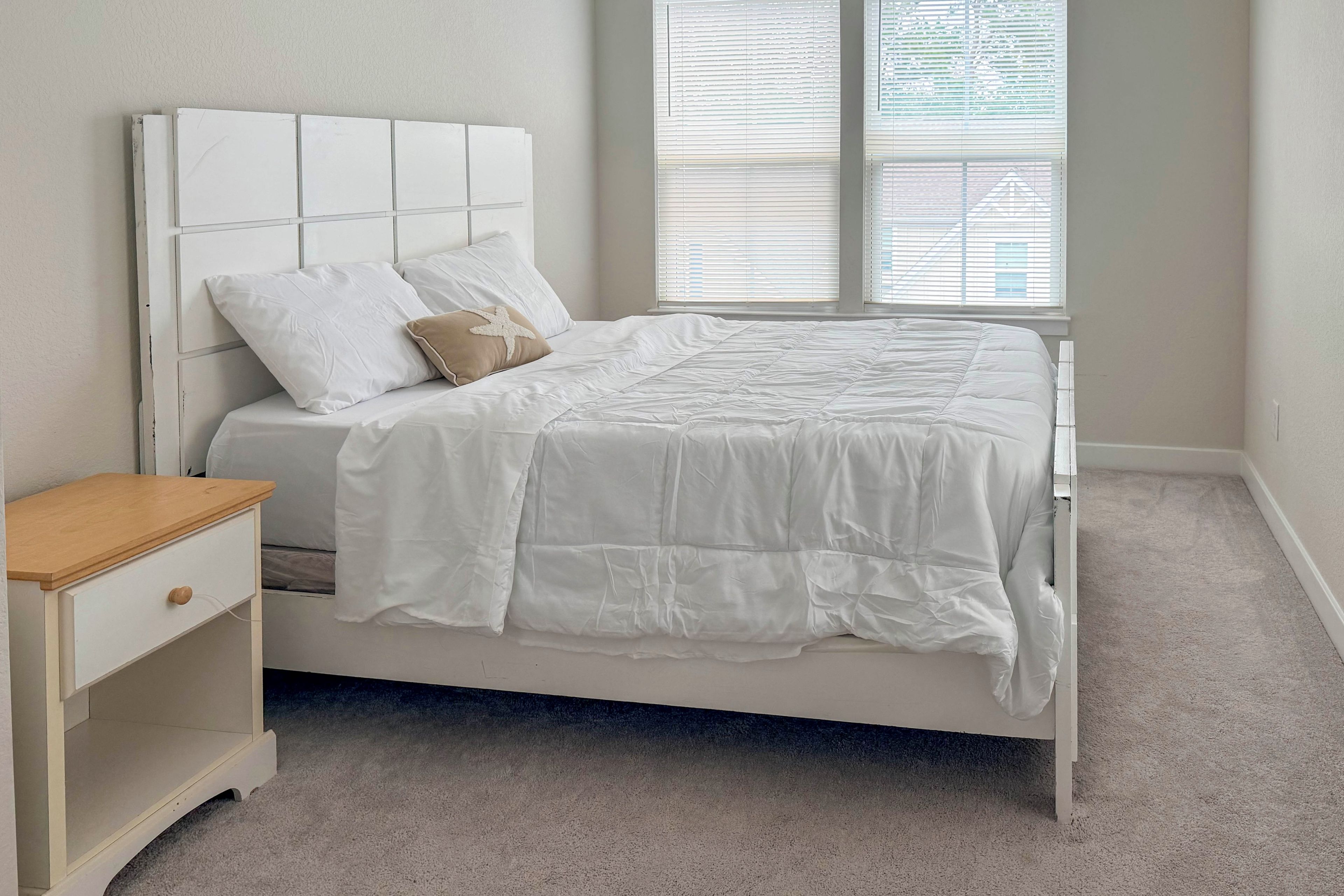A bedroom with a bed, a nightstand, and a window with blinds.