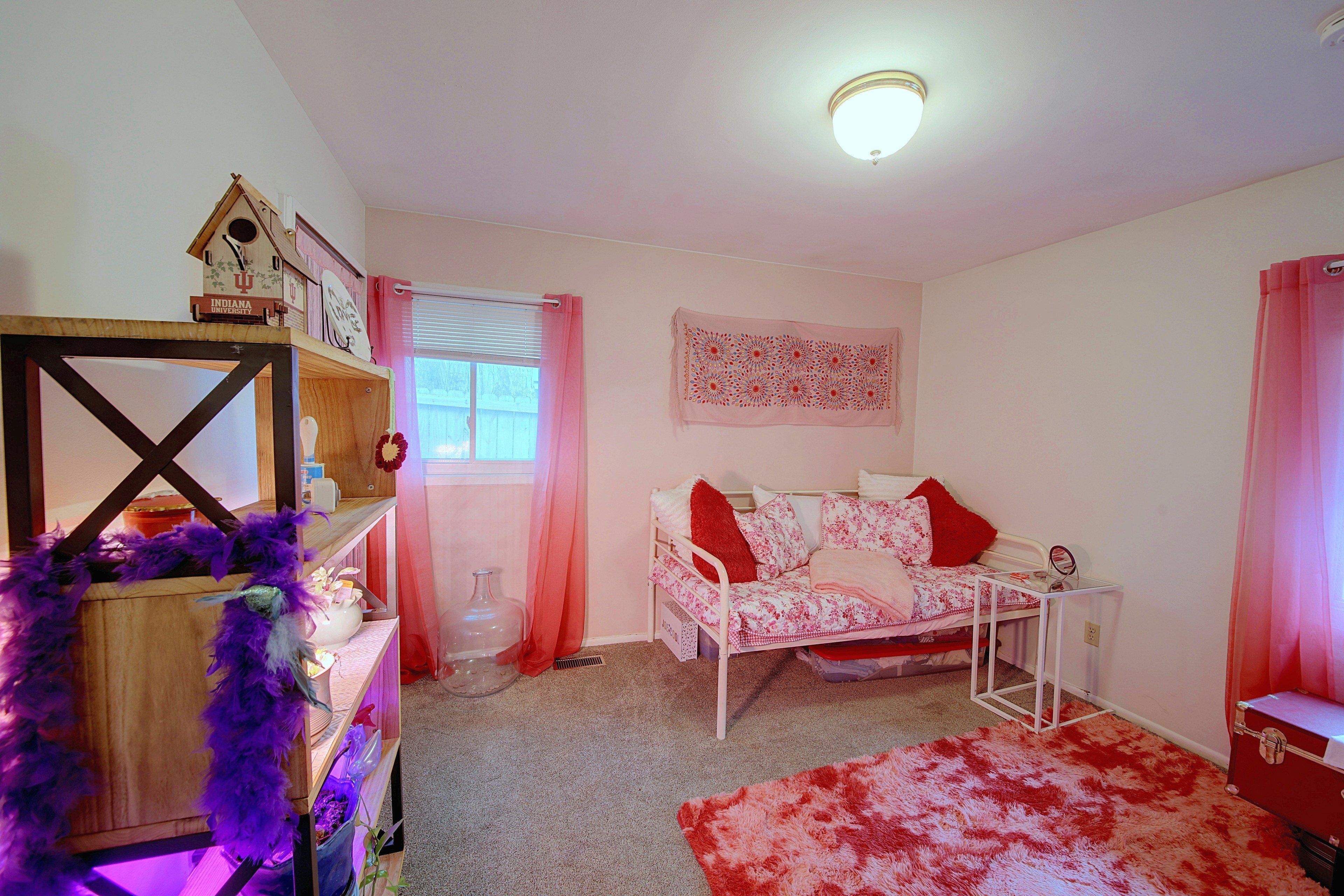 A room with a bed, a desk, a window with curtains, a wall clock, and a ceiling light.