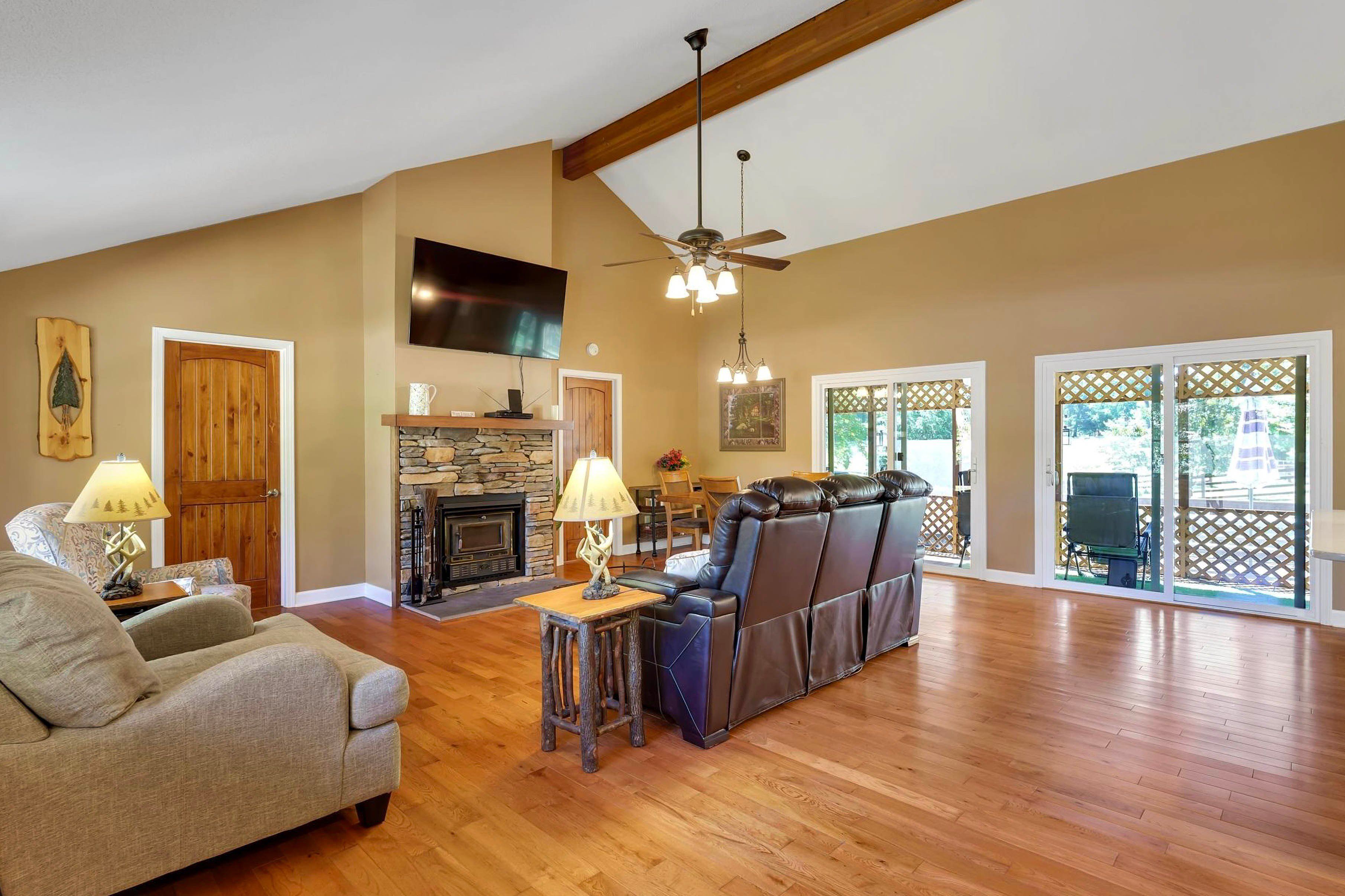 A spacious living room with a fireplace, a large leather sofa, and a television mounted on the wall.