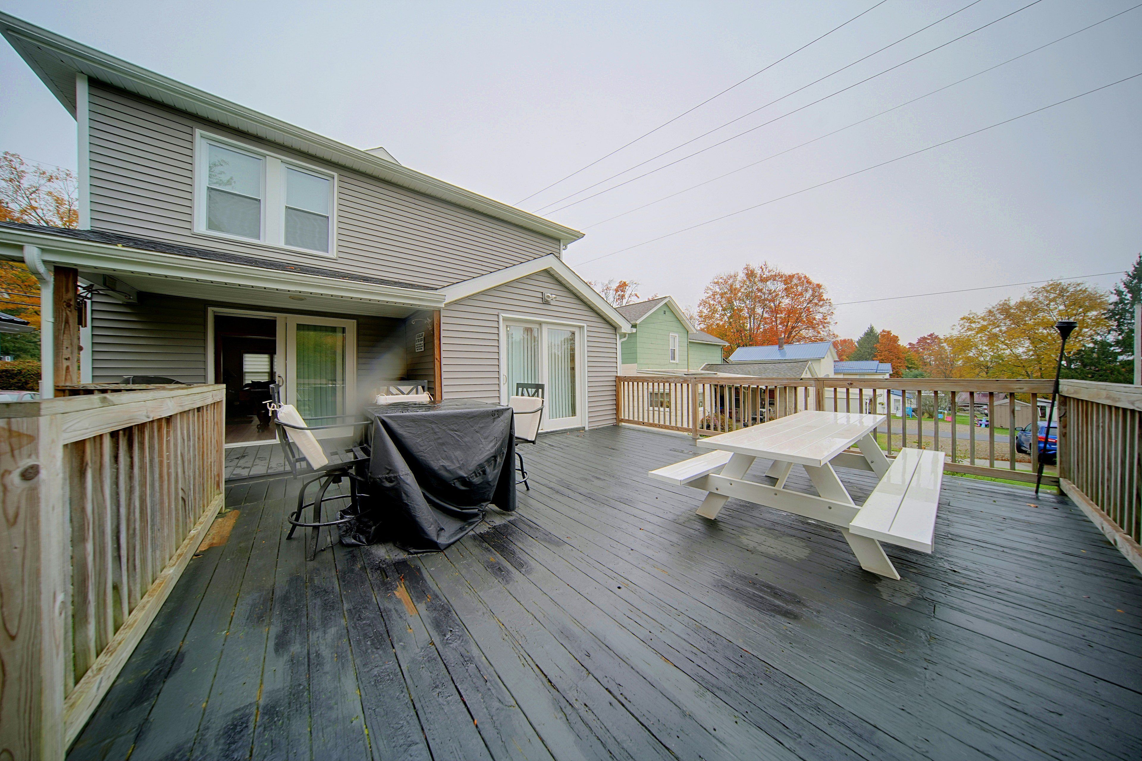 A covered deck with a picnic table and chairs, a grill, and a house with a front porch.