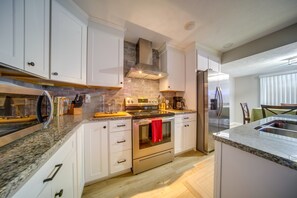 A modern kitchen with white cabinetry, a stainless steel refrigerator, and a granite countertop.