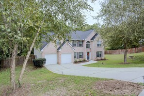 A two-story residential house with a brick facade, a front garage, and a well-maintained lawn.