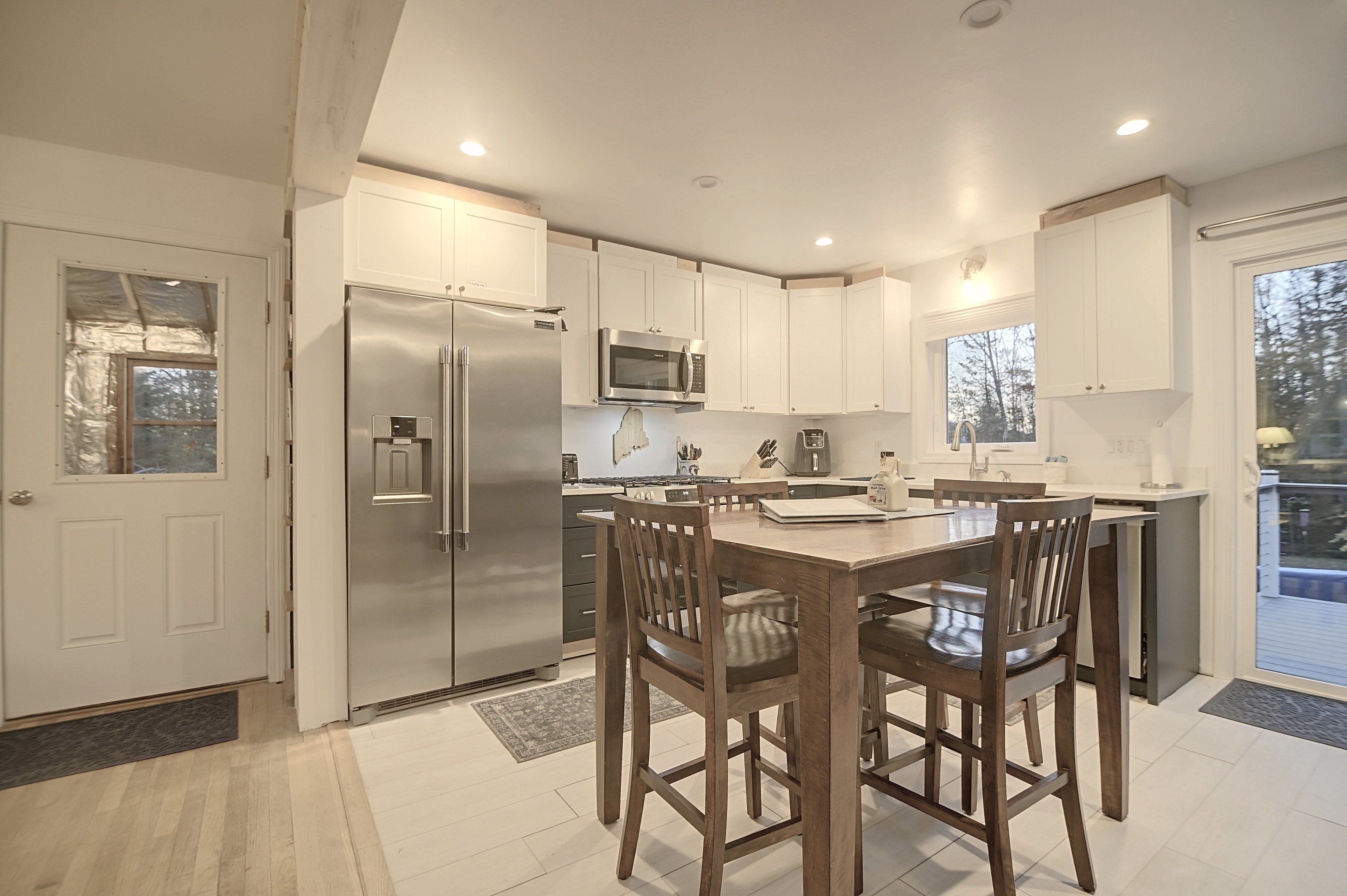 A modern kitchen with a stainless steel refrigerator, microwave, and stove, wooden chairs at a table, and white cabinetry.