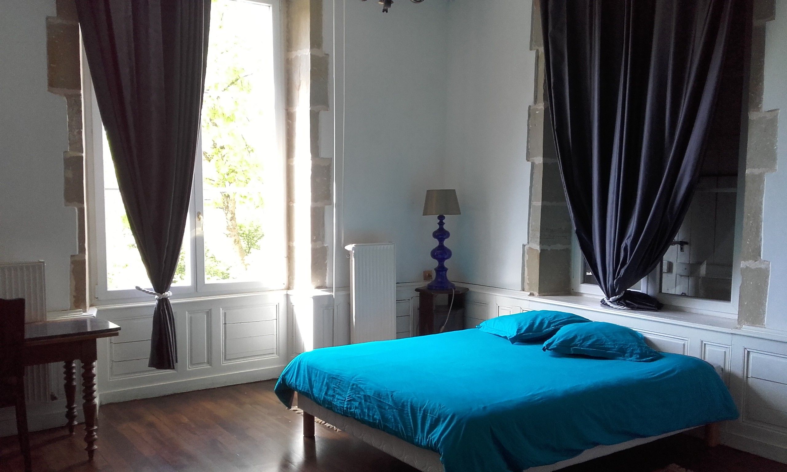 Un dormitorio con cama, una silla, una lámpara y un ventanal con cortinas.