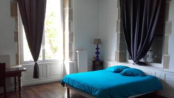 Un dormitorio con cama, una silla, una lámpara y un ventanal con cortinas.