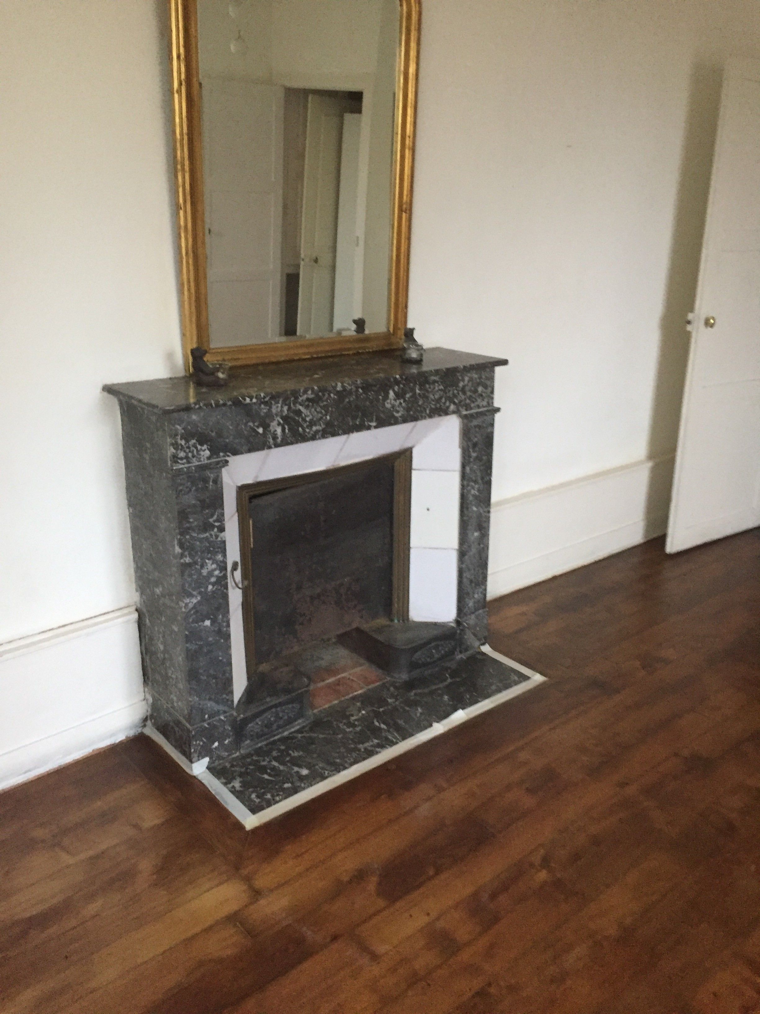 Een kamer met een open haard, een spiegel erboven en houten vloeren.