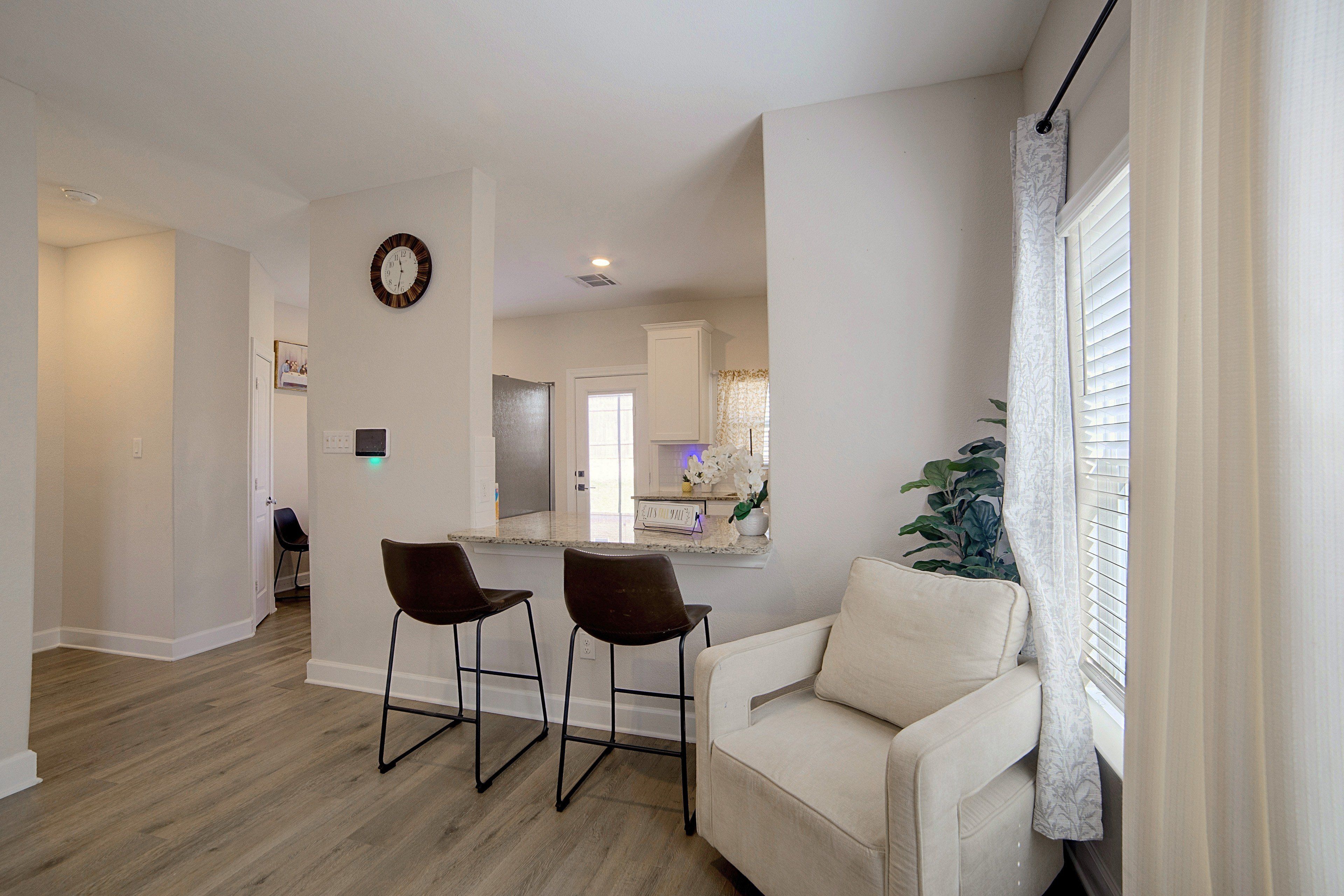 A modern kitchen with a marble countertop, two bar stools, a white sofa, and a potted plant.