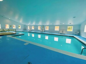 Una piscina interior amb aigua cristal·lina, envoltada de cadires blanques i finestres.