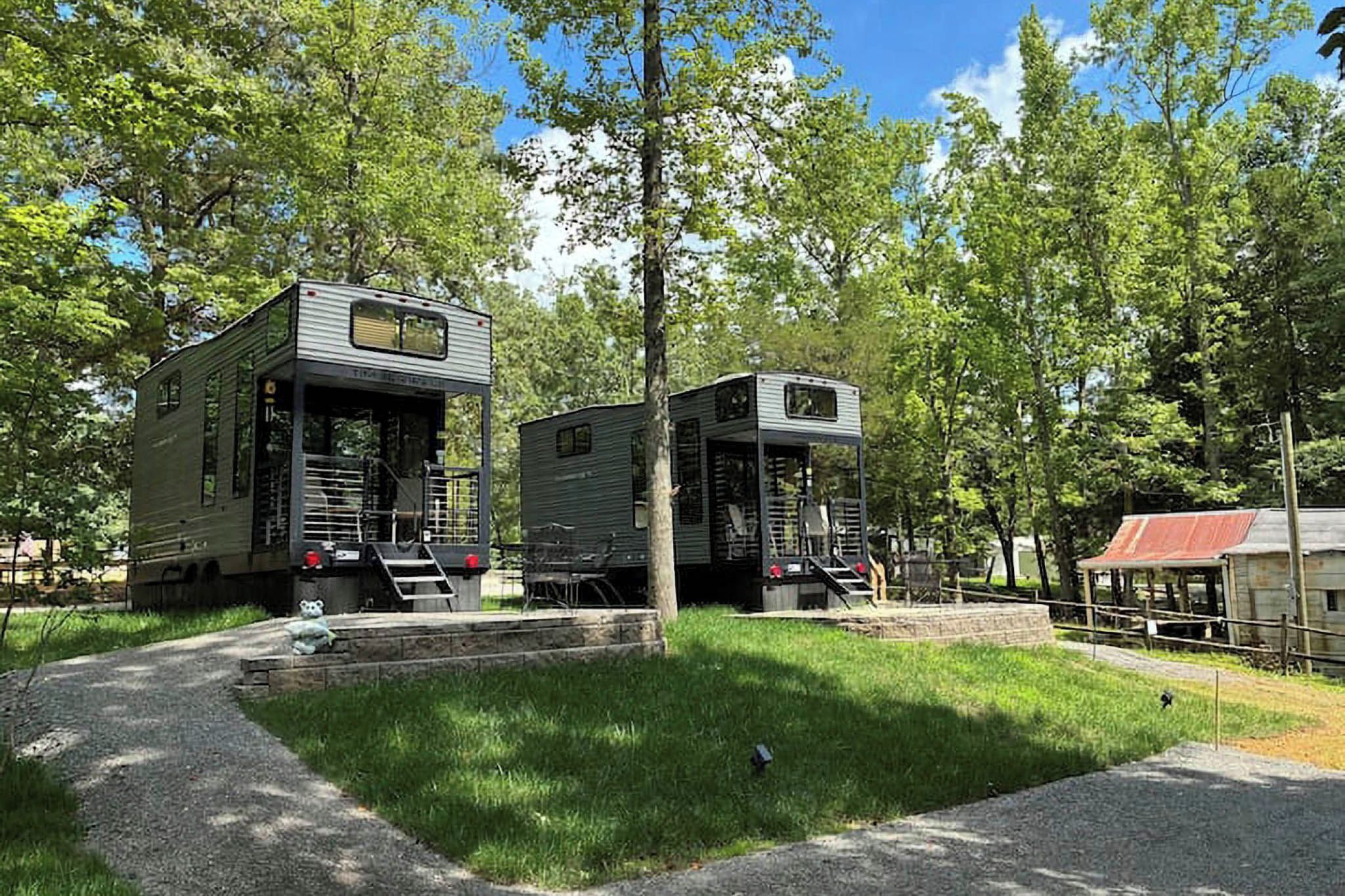 Two mobile homes with external staircases, surrounded by trees and a gravel path.