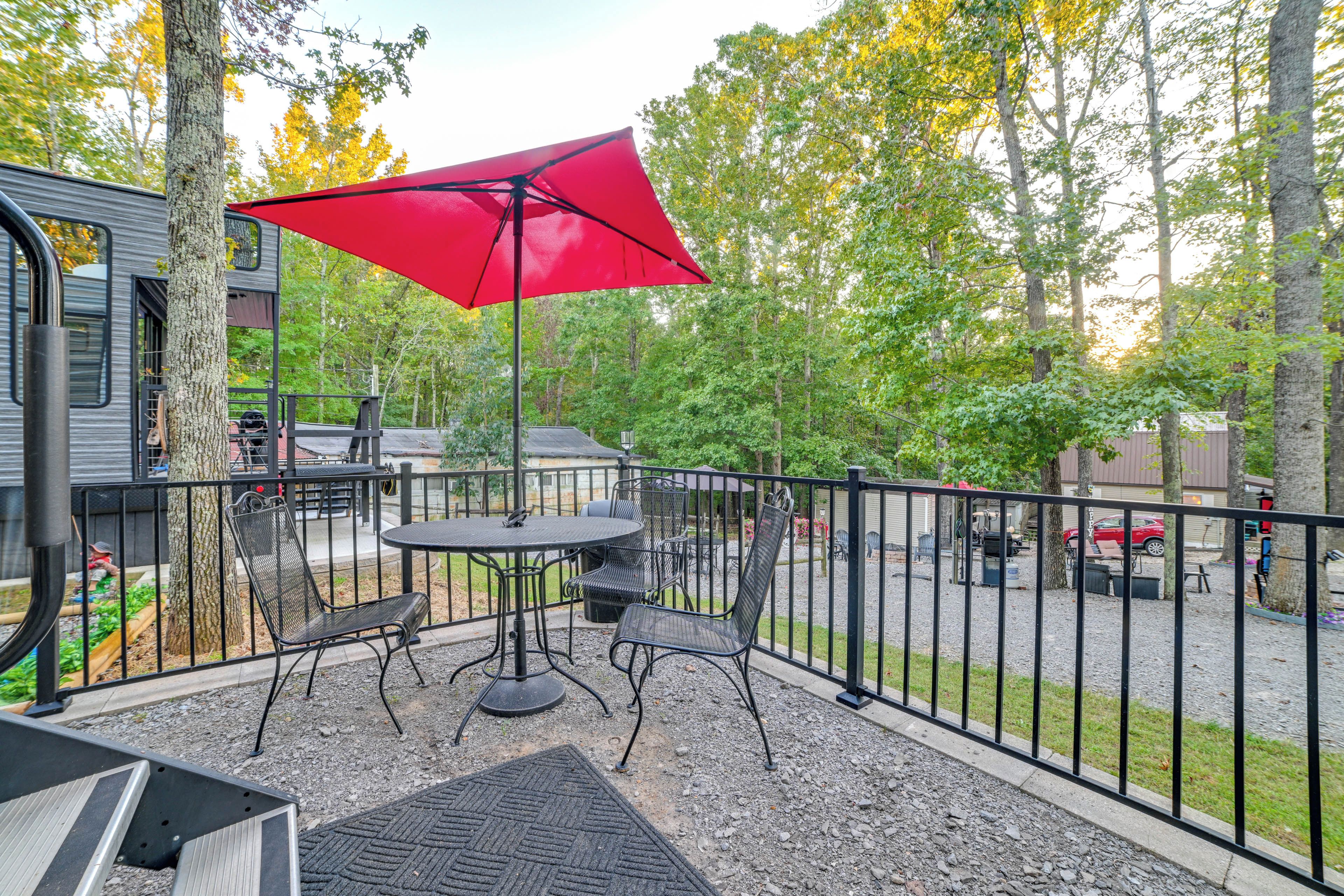 An outdoor patio with a table and chairs, a red umbrella, and a view of the surrounding trees and buildings.