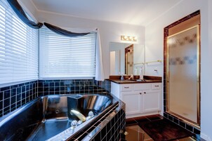 Un baño moderno con una bañera negra, muebles blancos y un espejo grande.