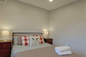 A neatly made bed with a checkered pillow, two bedside lamps, and a pair of towels on the floor.
