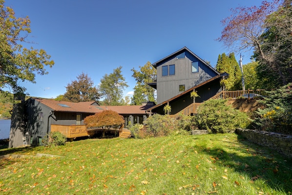 A two-story house with a sloped roof, a wooden deck, and a stone wall.