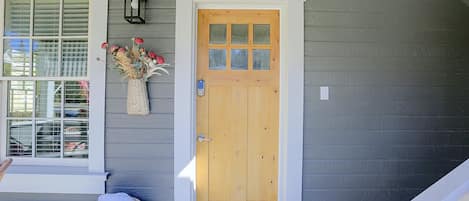 A wooden front door with a glass panel, a white-framed window, and a basket with a cushion on the porch.