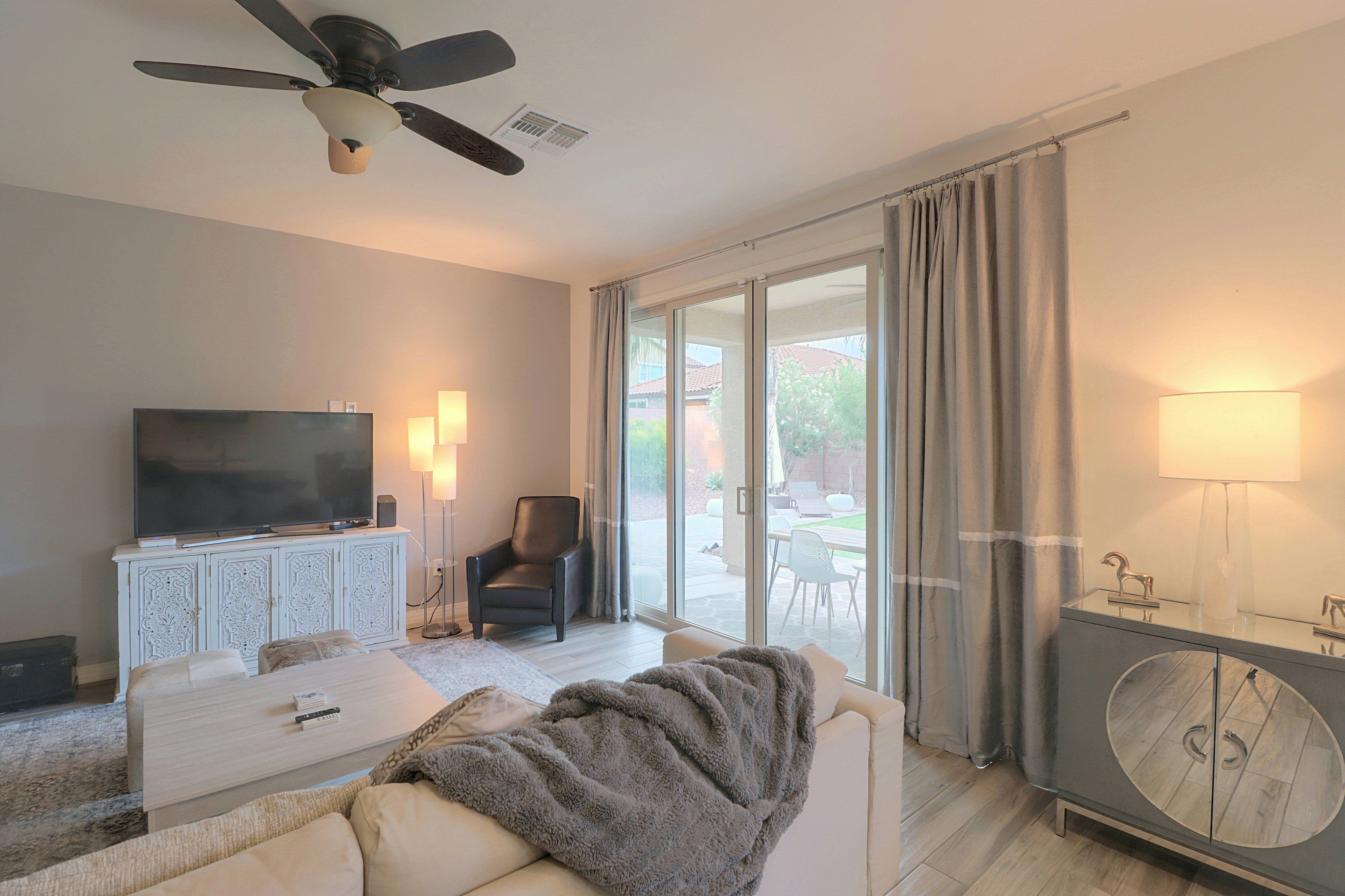 Sala de estar moderna com televisão de tela plana, ventilador de teto, sofá, mesa de centro e porta de vidro deslizante que dá para um pátio externo.