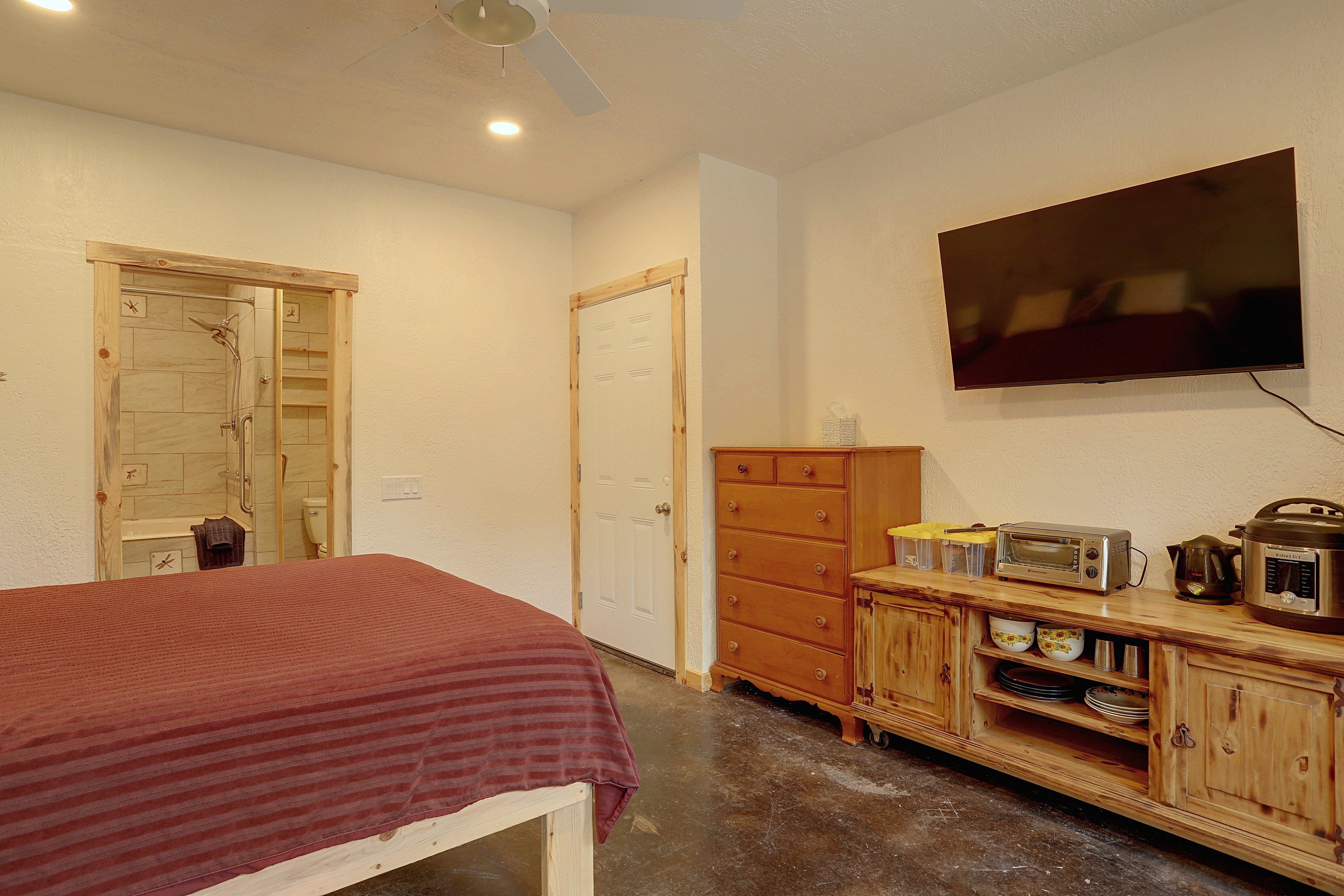 Quarto com cama, cômoda, televisão e chuveiro.