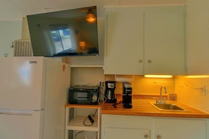 Una kitchenette compacta con microondas, cafetera y un pequeño estante.