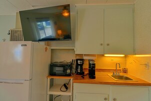 Una kitchenette compacta con microondas, cafetera y un pequeño estante.