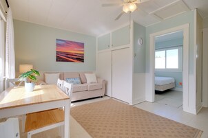 Una habitación con cama, sofá, mesa de comedor, ventilador de techo y un cuadro de un atardecer.