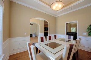 A dining area with a glass-top table and white upholstered chairs.