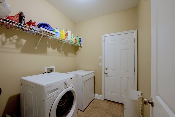 A laundry room with two washing machines, a shelf with cleaning supplies, and a closed door.