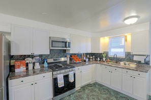 A modern kitchen with white cabinets, a stainless steel stove, a microwave, and a sink.